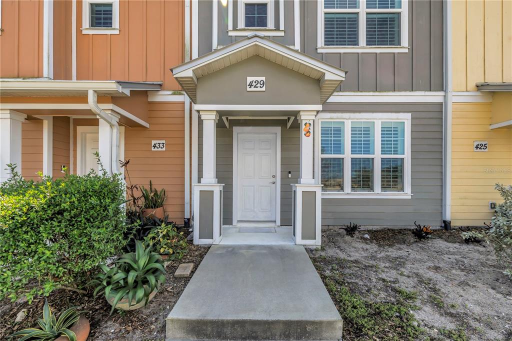 The exterior of a multi-unit townhouse features a covered entryway with a white front door — 429 LORRAINE LELAND STREET, DUNEDIN, FL