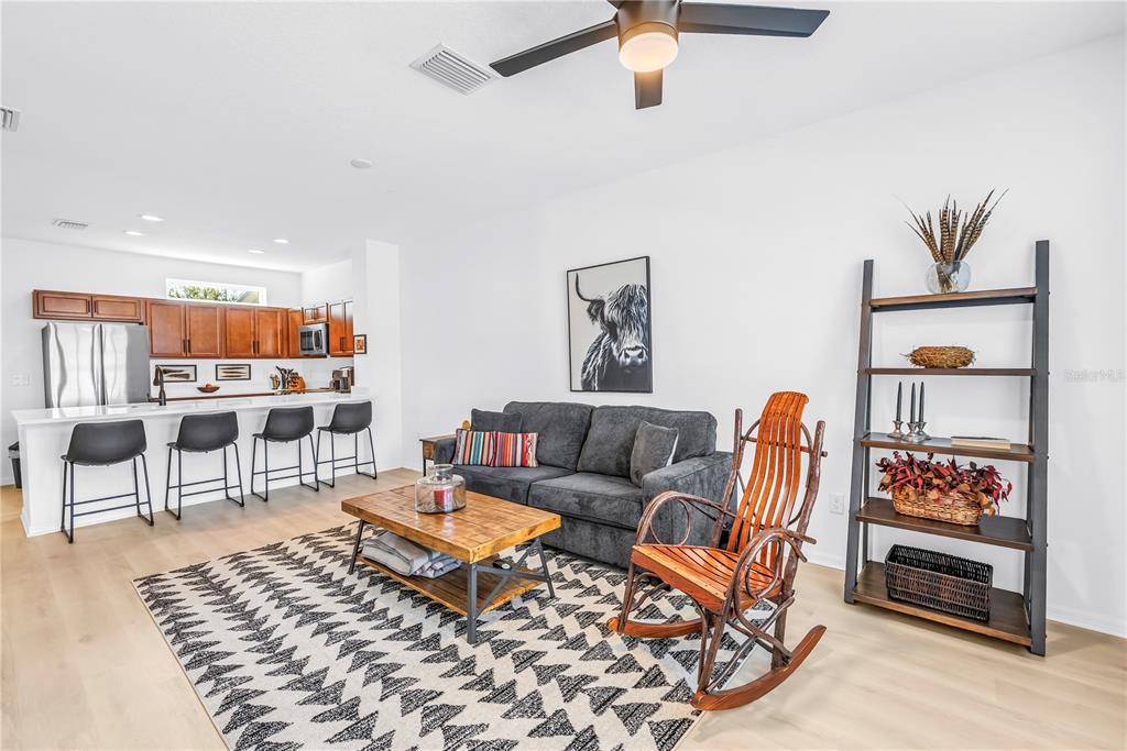 A living room with a gray sofa, wooden rocking chair, and an open kitchen area — 429 LORRAINE LELAND STREET, DUNEDIN, FL