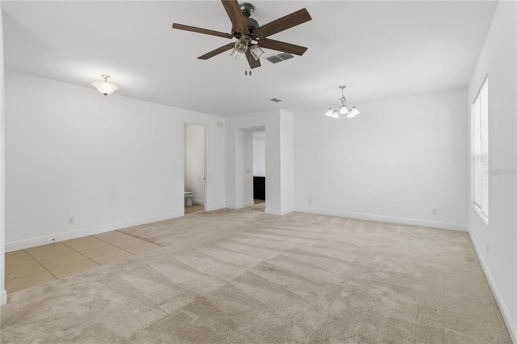 A spacious room with beige carpet, white walls, a ceiling fan, and a chandelier — 3393 WAUSEON DRIVE, ST CLOUD, FL