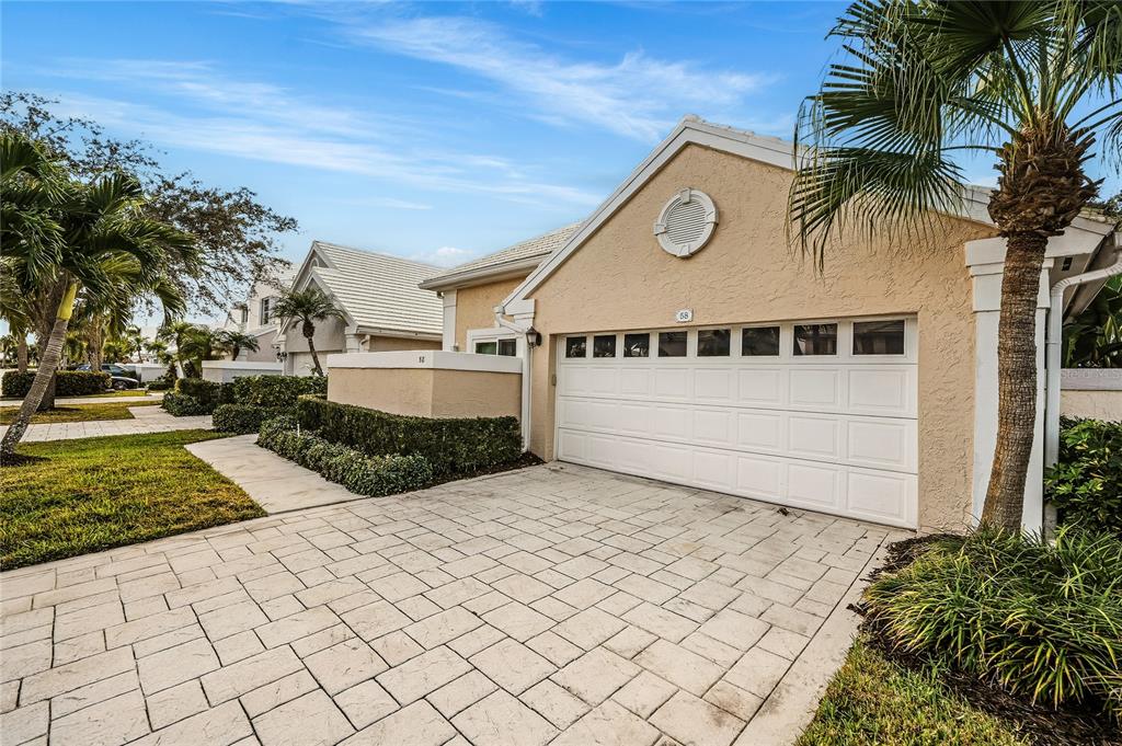 A beige house with a white garage door and a paved driveway under a blue sky — 58 WINDSOR LANE, PALM BEACH GARDENS, FL