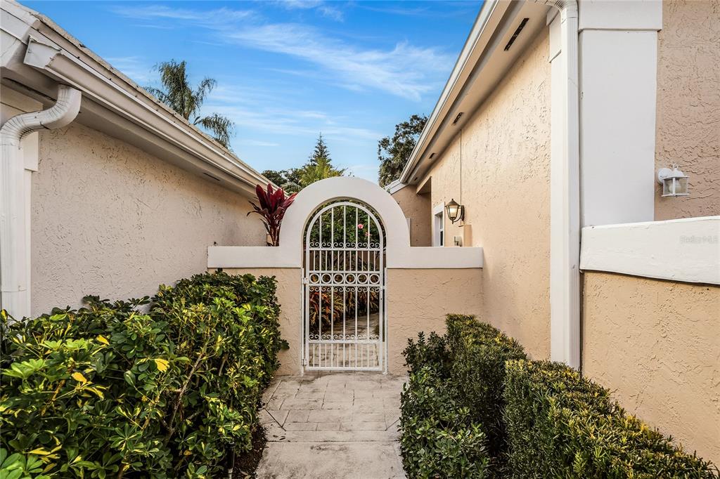 A white arched gate leads to a courtyard between two stucco exterior walls — 58 WINDSOR LANE, PALM BEACH GARDENS, FL
