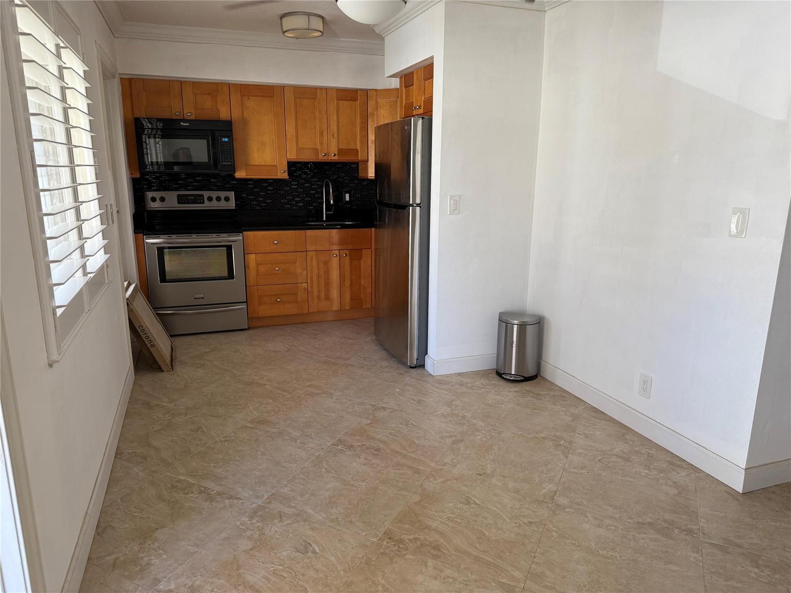 A kitchen features wood cabinets, stainless steel appliances, black countertops, and light-colored tile flooring — 2131 NE 42nd Court # 202e, Lighthouse Point FL 33064, LIGHTHOUSE POINT, FL