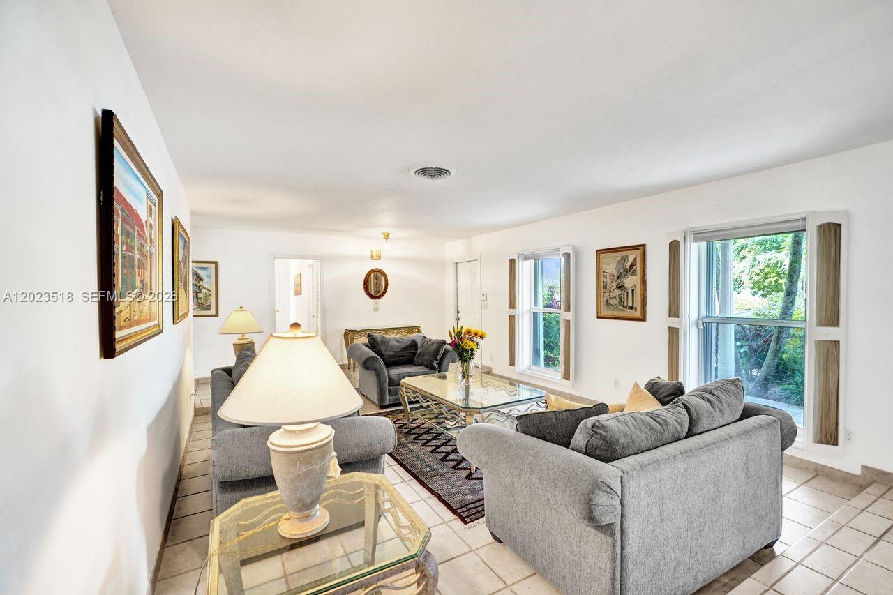 A living room features gray sofas, a glass coffee table, tile flooring, and windows — 8521 SW 86th Ct, Miami FL 33143, MIAMI, FL