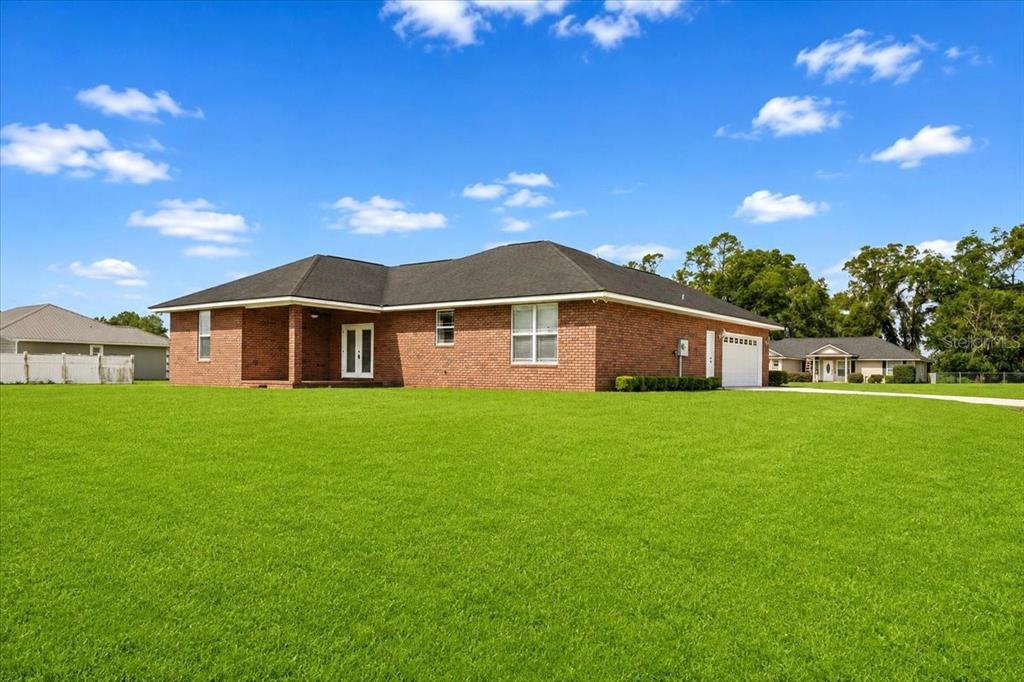 A single-story brick house with a dark shingled roof sits on a large grassy lawn — 122 SW ARROW GLEN, LAKE CITY, FL