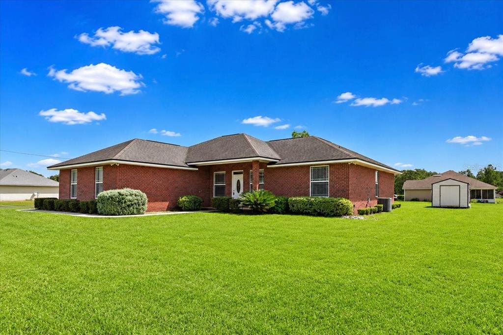A single-story red brick house with a dark shingled roof sits on a grassy lawn — 122 SW ARROW GLEN, LAKE CITY, FL