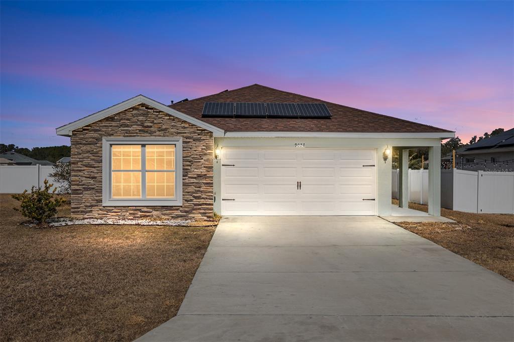 A single-story house with a stone facade, a two-car garage, and rooftop solar panels — 9074 SE 47TH COURT ROAD, OCALA, FL