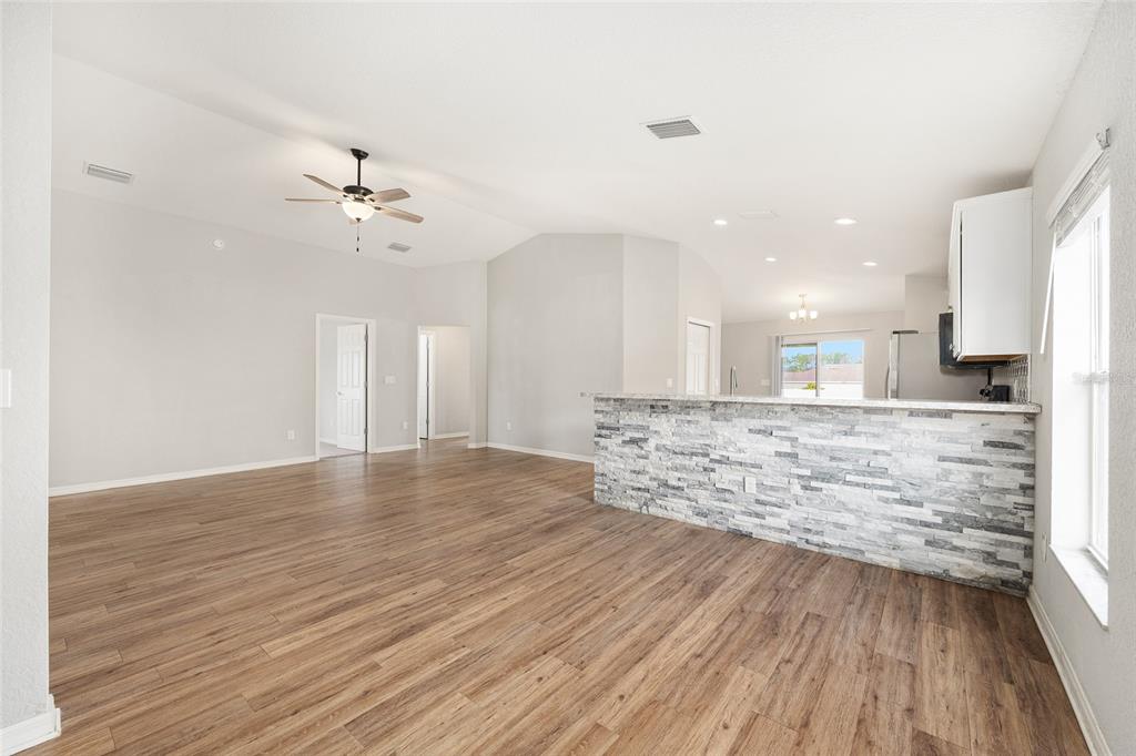 An open-concept living area features wood-look flooring, a vaulted ceiling, and a stone-accented breakfast bar — 9074 SE 47TH COURT ROAD, OCALA, FL