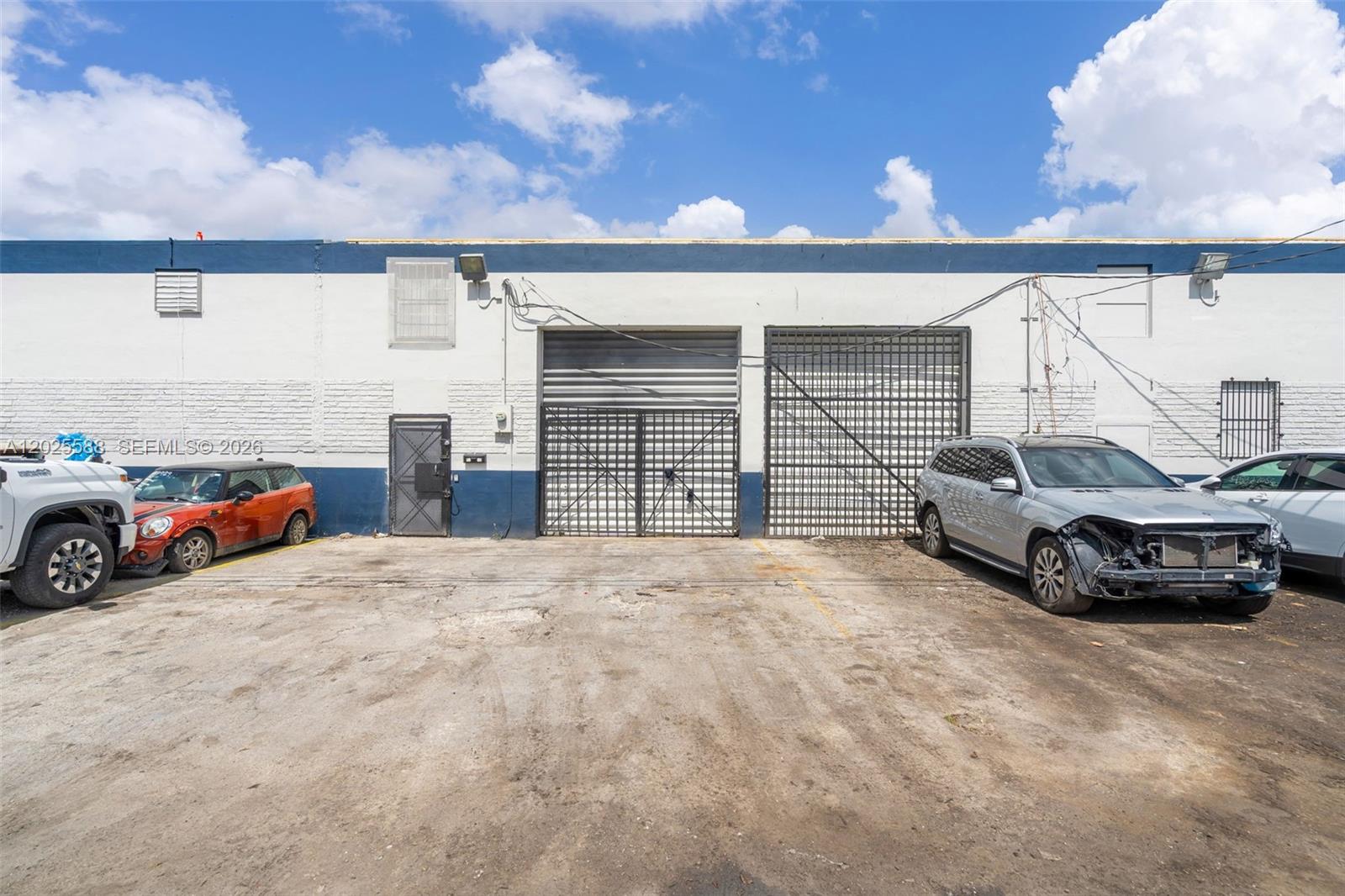 The exterior of a commercial warehouse building features two large roll-up doors and parked cars — 3500 NW 54th St # 5214, Miami FL 33142, MIAMI, FL