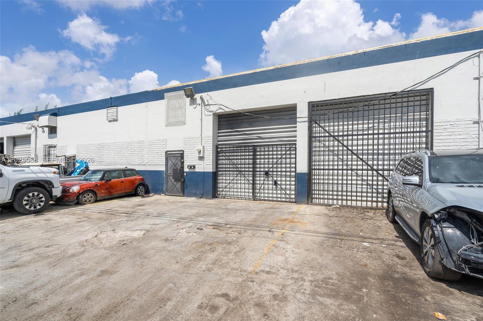 An exterior view of a commercial warehouse building with metal security gates and parked cars — 3500 NW 54th St # 5214, Miami FL 33142, MIAMI, FL