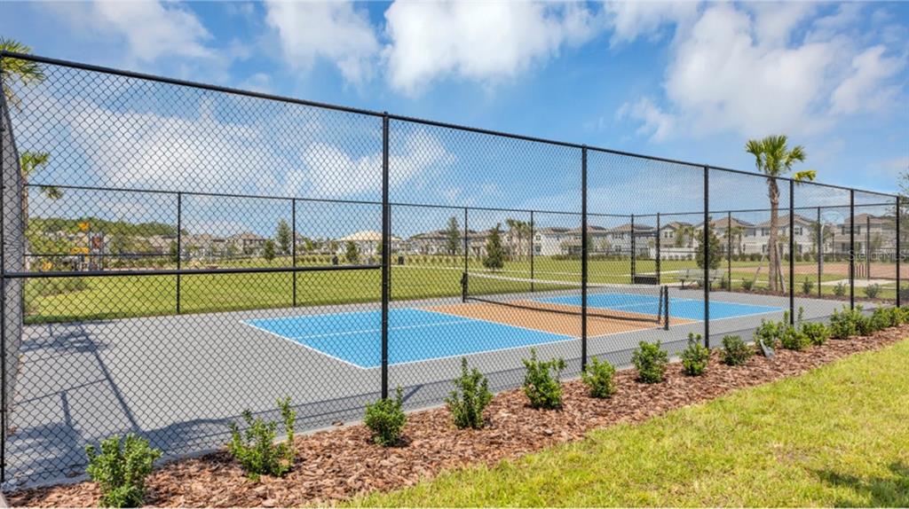 A fenced-in outdoor pickleball court with blue and grey surfacing sits on a grassy lot — 5579 MORANT BAY PATH, KISSIMMEE, FL