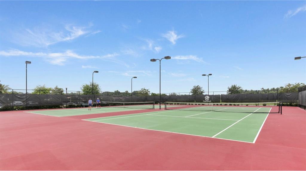 Two tennis courts with red and green surfaces are enclosed by a black fence — 5579 MORANT BAY PATH, KISSIMMEE, FL