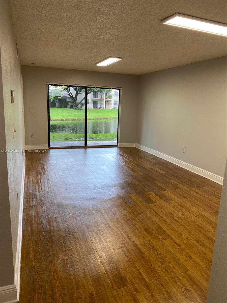 An empty room with wood-look flooring and a sliding glass door overlooking a pond — 9981 Nob Hill Ct # 9981, Sunrise FL 33351, SUNRISE, FL