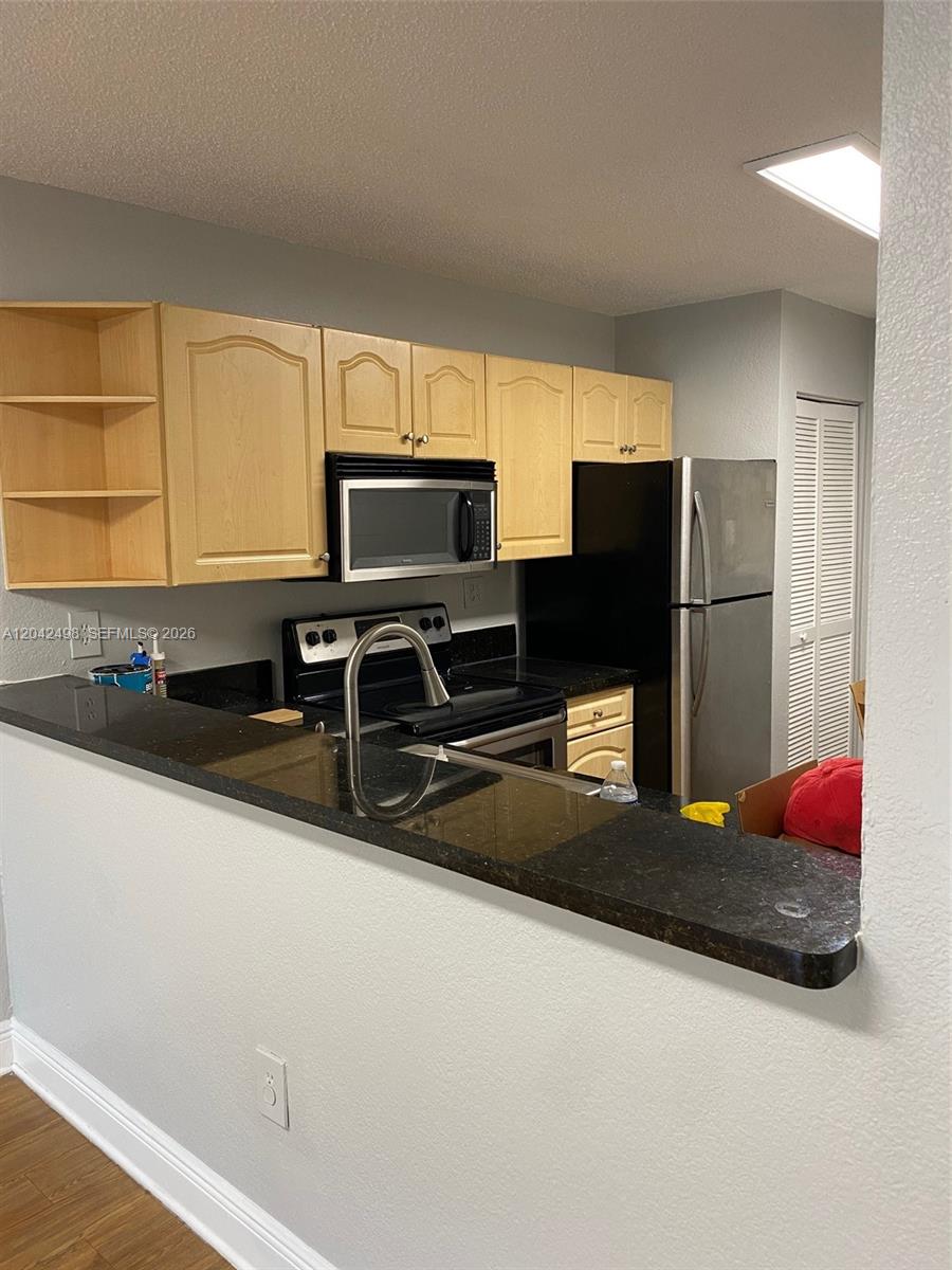 A kitchen features light wood cabinets, black countertops, and stainless steel appliances — 9981 Nob Hill Ct # 9981, Sunrise FL 33351, SUNRISE, FL