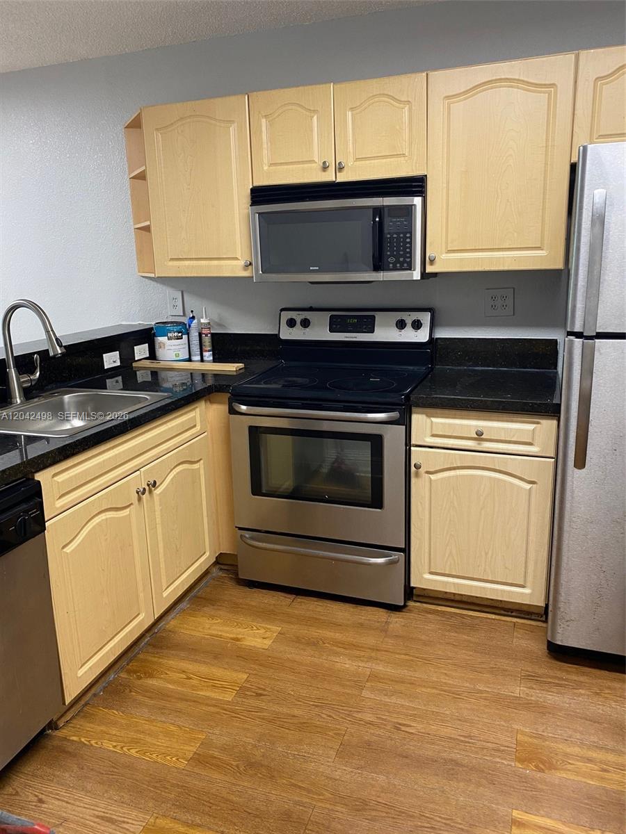 A kitchen features light wood cabinets, black countertops, stainless steel appliances, and wood-look flooring — 9981 Nob Hill Ct # 9981, Sunrise FL 33351, SUNRISE, FL