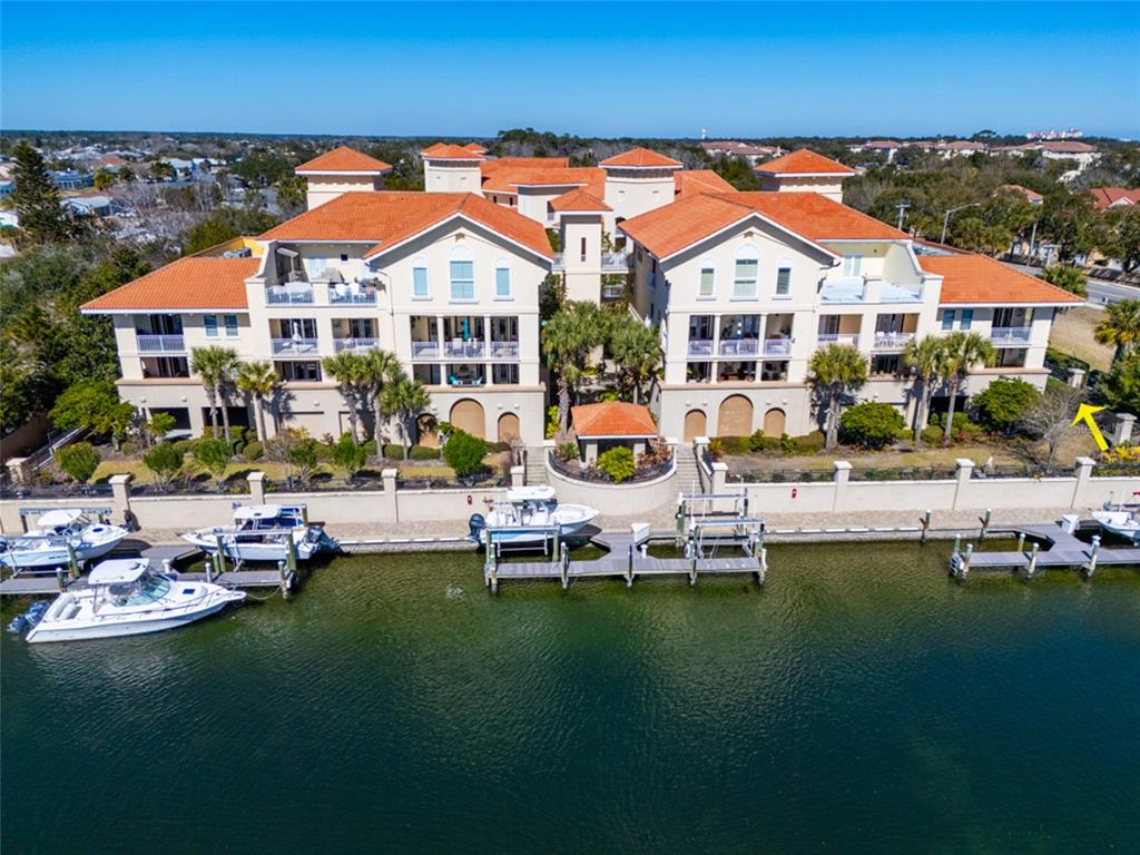 An aerial view shows a multi-story waterfront condominium building with a tiled roof and docks — 300 BELLA HARBOR COURT UNIT 101, PALM COAST, FL