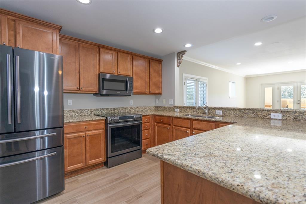 A kitchen features wood cabinets, granite countertops, stainless steel appliances, and light wood flooring — 300 BELLA HARBOR COURT UNIT 101, PALM COAST, FL