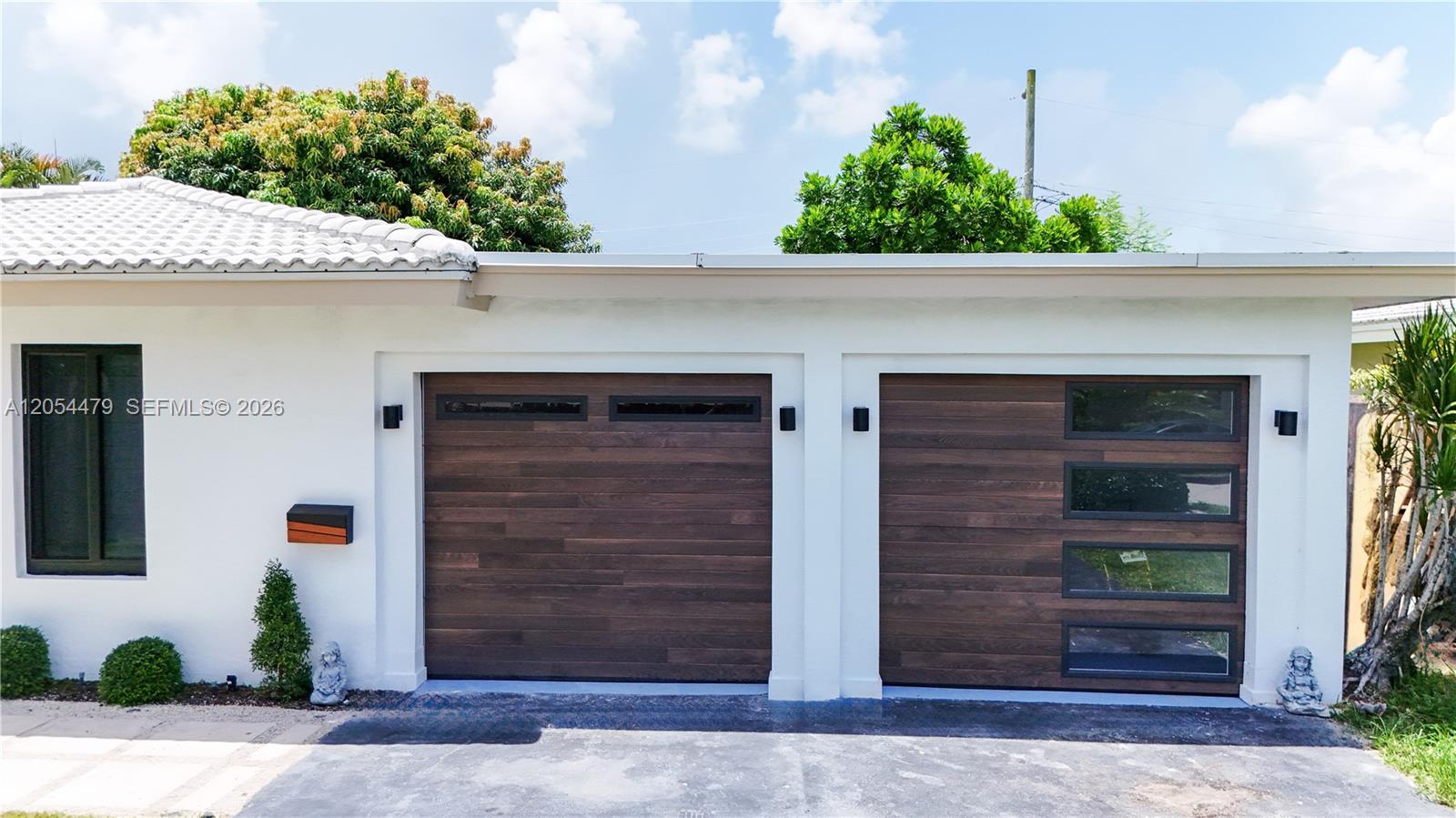 The exterior view shows a white house with two modern wood-paneled garage doors — 1892 NE 33rd St, Oakland Park FL 33306, OAKLAND PARK, FL