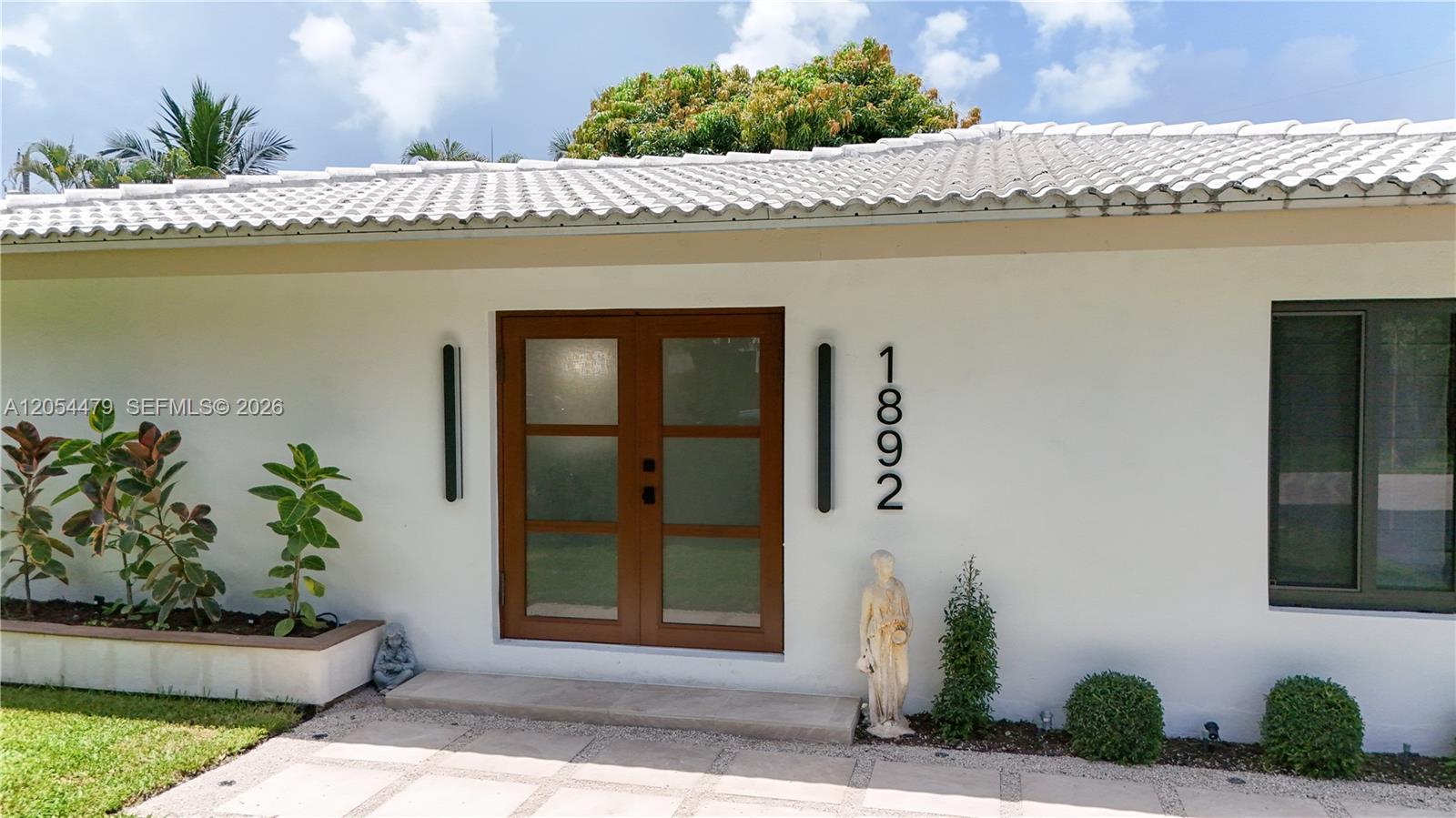 A white house exterior features a double wooden door, modern lighting, and a stone walkway — 1892 NE 33rd St, Oakland Park FL 33306, OAKLAND PARK, FL