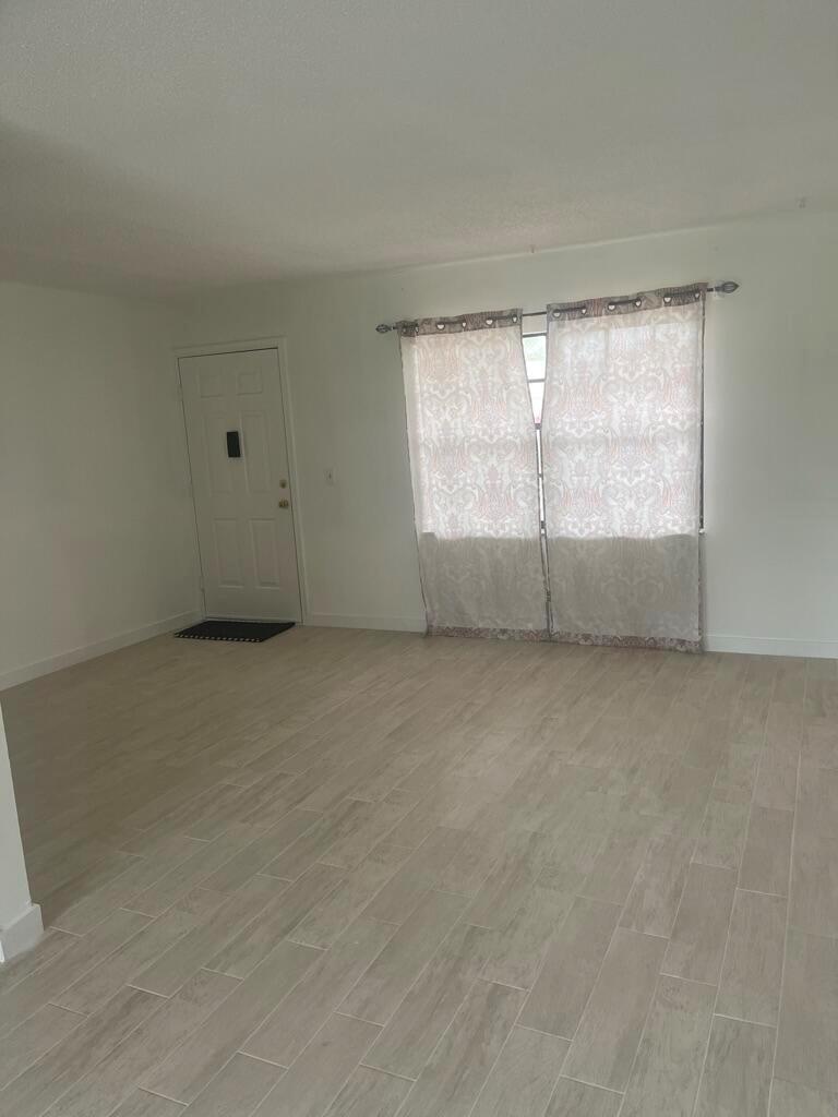 A living room with white walls, light wood-look tile flooring, and a window with curtains — 4259 Oak Terrace Drive, FL 33463, FL