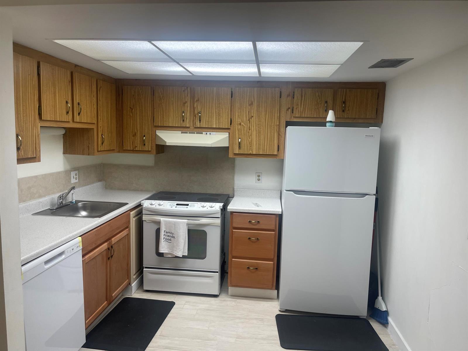 A kitchen features wood cabinets, white appliances, laminate countertops, and a drop ceiling light panel — 4259 Oak Terrace Drive, FL 33463, FL