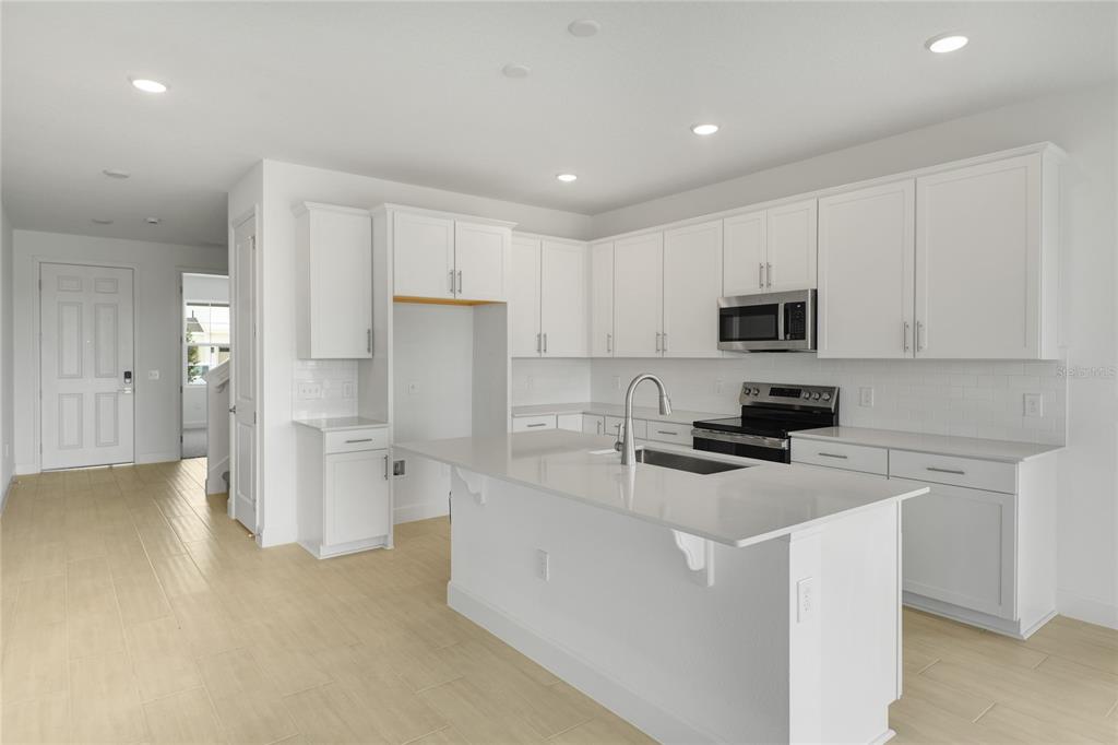 A modern kitchen features white cabinets, a central island with a sink, and light-colored flooring — 1698 CROOKED CREEK STREET, ST CLOUD, FL