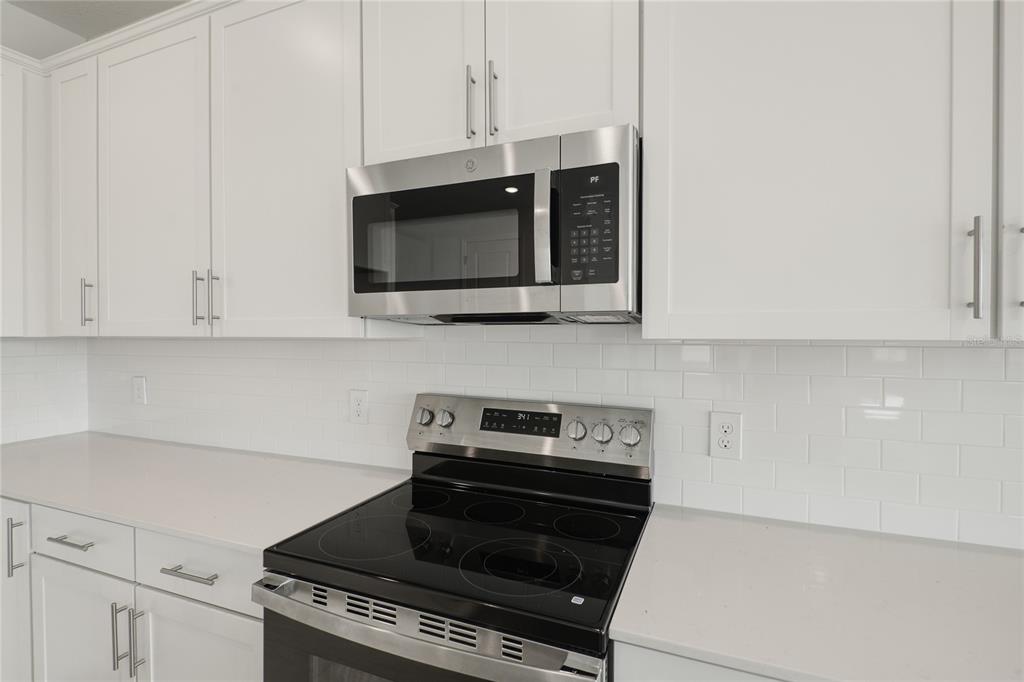A modern kitchen features white cabinets, a stainless steel microwave, and a glass-top electric range — 1698 CROOKED CREEK STREET, ST CLOUD, FL