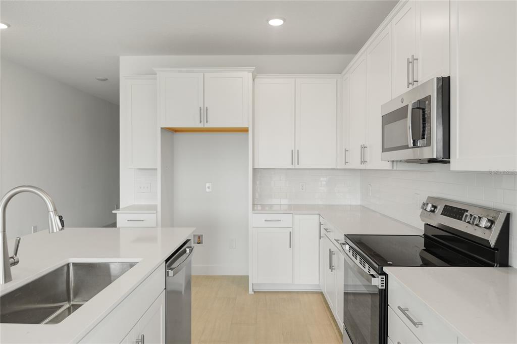 A modern kitchen features white cabinets, stainless steel appliances, and a central island with a sink — 1698 CROOKED CREEK STREET, ST CLOUD, FL