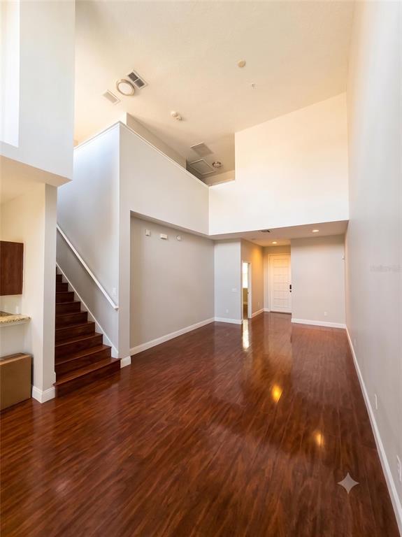 A bright living area features high ceilings, dark wood flooring, and a staircase with wooden steps — 10158 RIDGEBLOOM AVENUE, ORLANDO, FL