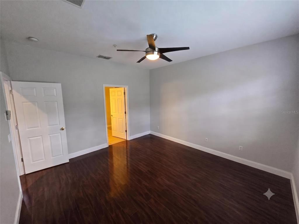A bedroom features dark wood-look flooring, light gray walls, and a ceiling fan — 10158 RIDGEBLOOM AVENUE, ORLANDO, FL
