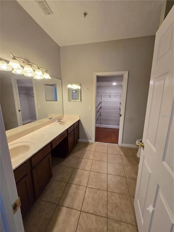 A bathroom features a double vanity with dark cabinets, a large mirror, and a walk-in closet — 10158 RIDGEBLOOM AVENUE, ORLANDO, FL