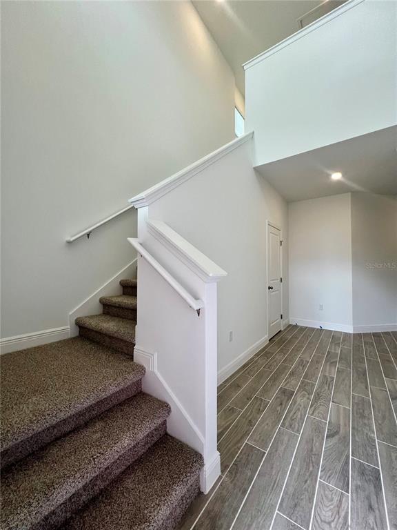 A carpeted staircase with a white railing leads upward next to a wood-look tiled hallway — 2241 JUNIPER BERRY DRIVE, MINNEOLA, FL