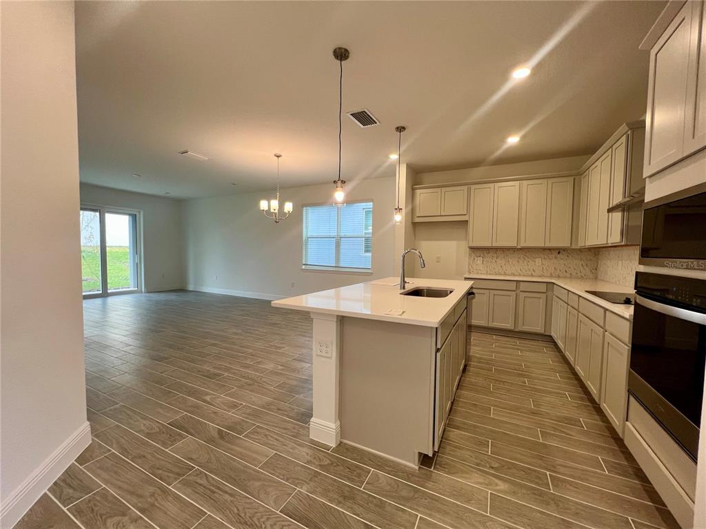 An open-concept kitchen with light-colored cabinets and a central island overlooks a spacious living area — 2241 JUNIPER BERRY DRIVE, MINNEOLA, FL