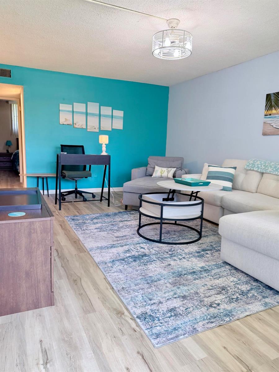 A living room features a teal accent wall, a white sectional sofa, and a patterned rug — 2400 NE 10th Street # 106, Pompano Beach FL 33062, POMPANO BEACH, FL