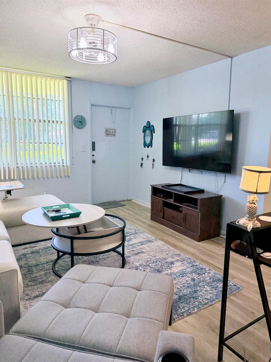 A living room features a wall-mounted television, a coffee table, and a light-colored sofa — 2400 NE 10th Street # 106, Pompano Beach FL 33062, POMPANO BEACH, FL
