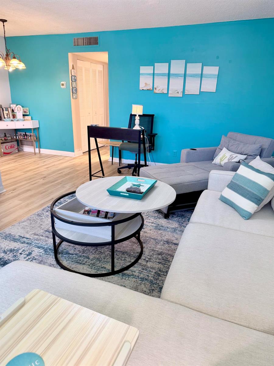 A living room features a bright turquoise wall, a sectional sofa, and a round coffee table — 2400 NE 10th Street # 106, Pompano Beach FL 33062, POMPANO BEACH, FL