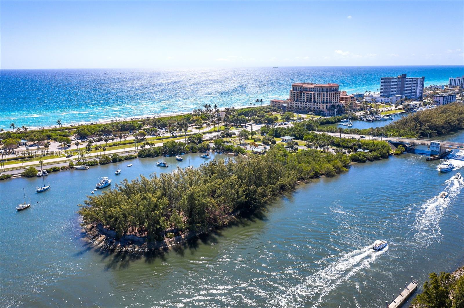 An aerial view shows a lush island surrounded by water with boats, a bridge, and coastal buildings — HOLLYWOOD, FL