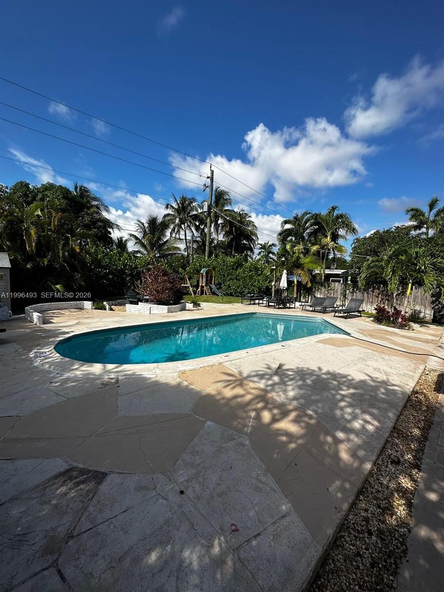 A backyard features a kidney-shaped swimming pool surrounded by a stone patio and palm trees — 1448 Dewey St # 1448, Hollywood FL 33020, HOLLYWOOD, FL