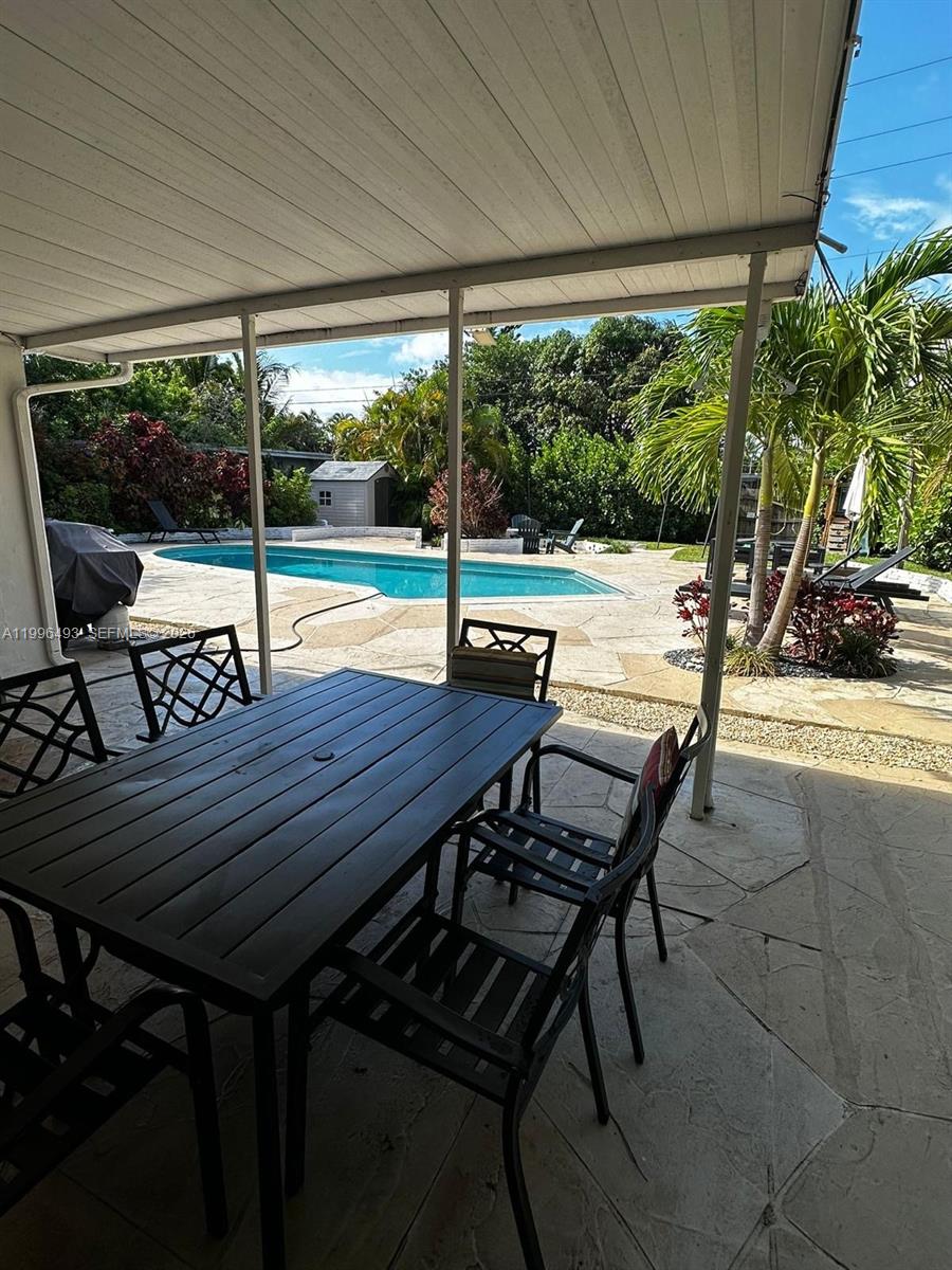 A covered patio with a dining set overlooks a backyard swimming pool and landscaping — 1448 Dewey St # 1448, Hollywood FL 33020, HOLLYWOOD, FL