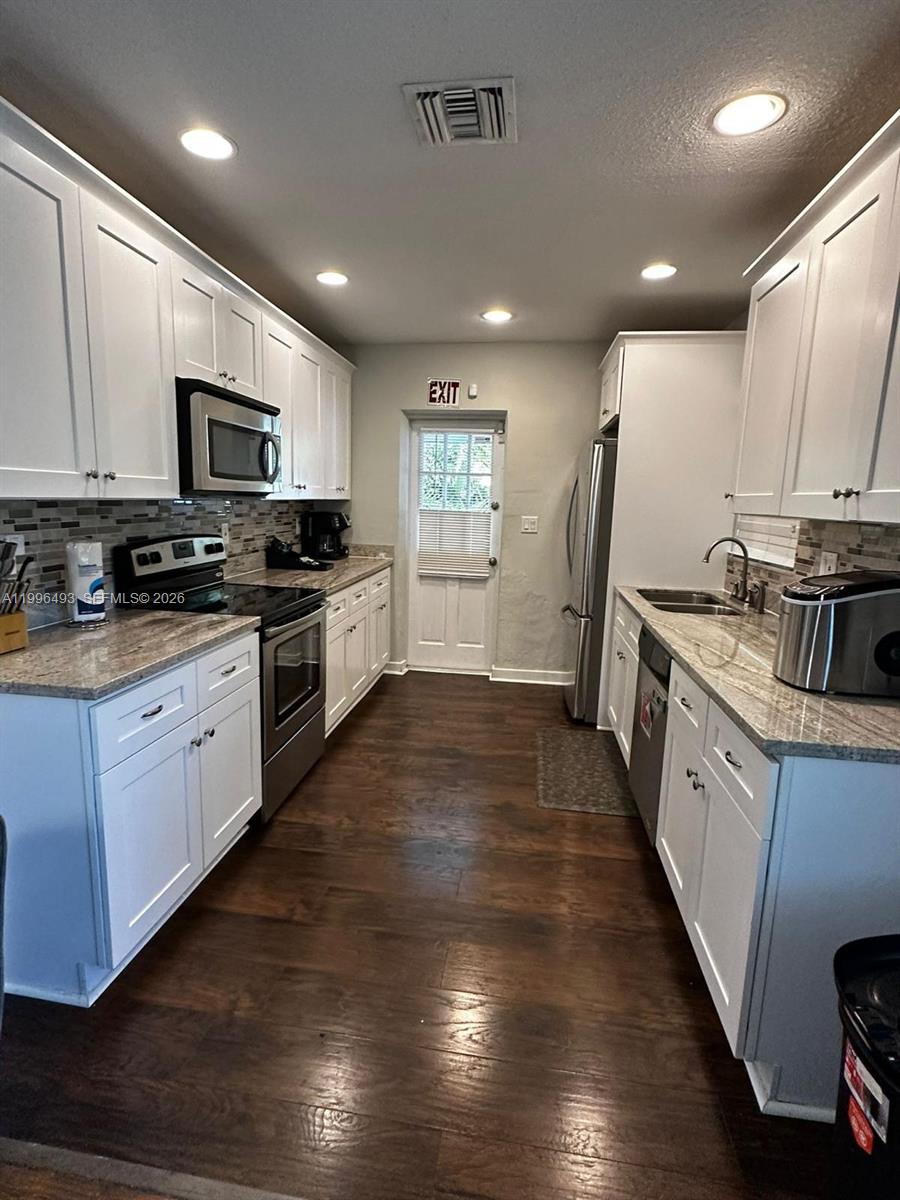 A galley kitchen features white cabinets, granite countertops, stainless steel appliances, and dark wood flooring — 1448 Dewey St # 1448, Hollywood FL 33020, HOLLYWOOD, FL