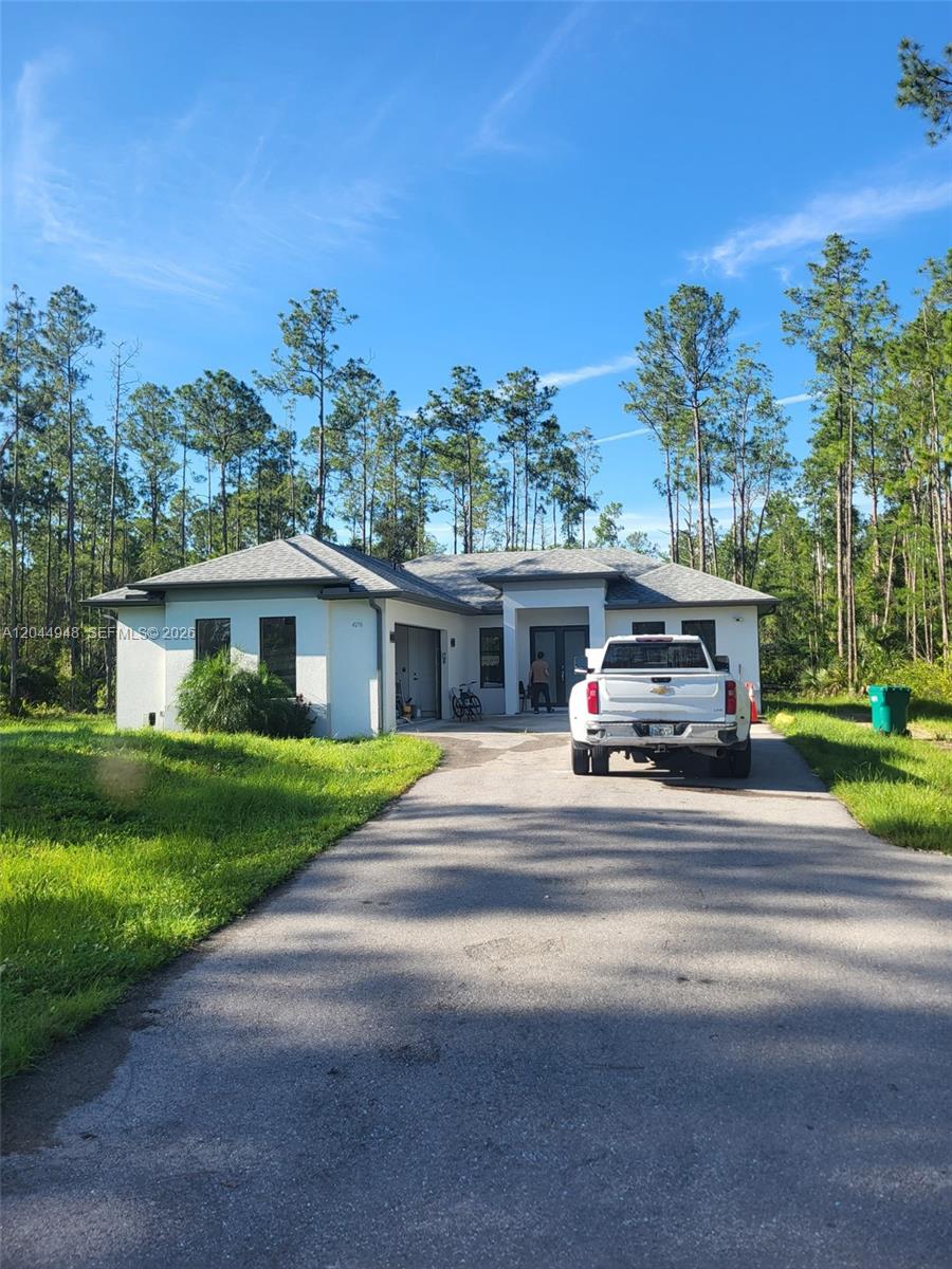A white single-story house with a gray roof and a driveway sits among pine trees — 4276 12th Avenue, Naples FL 34120, NAPLES, FL