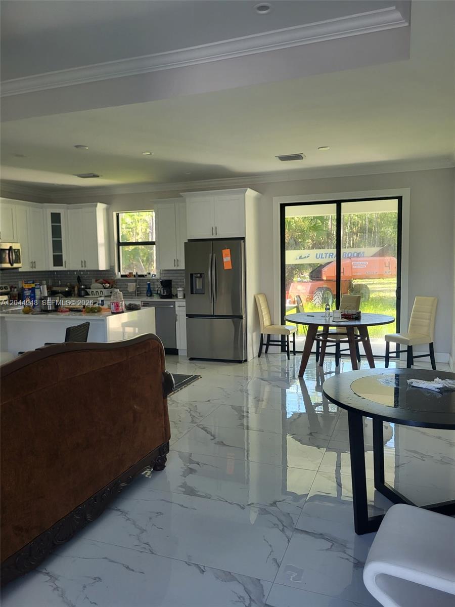 A kitchen and dining area with white cabinets, stainless steel appliances, and glossy marble-look flooring — 4276 12th Avenue, Naples FL 34120, NAPLES, FL