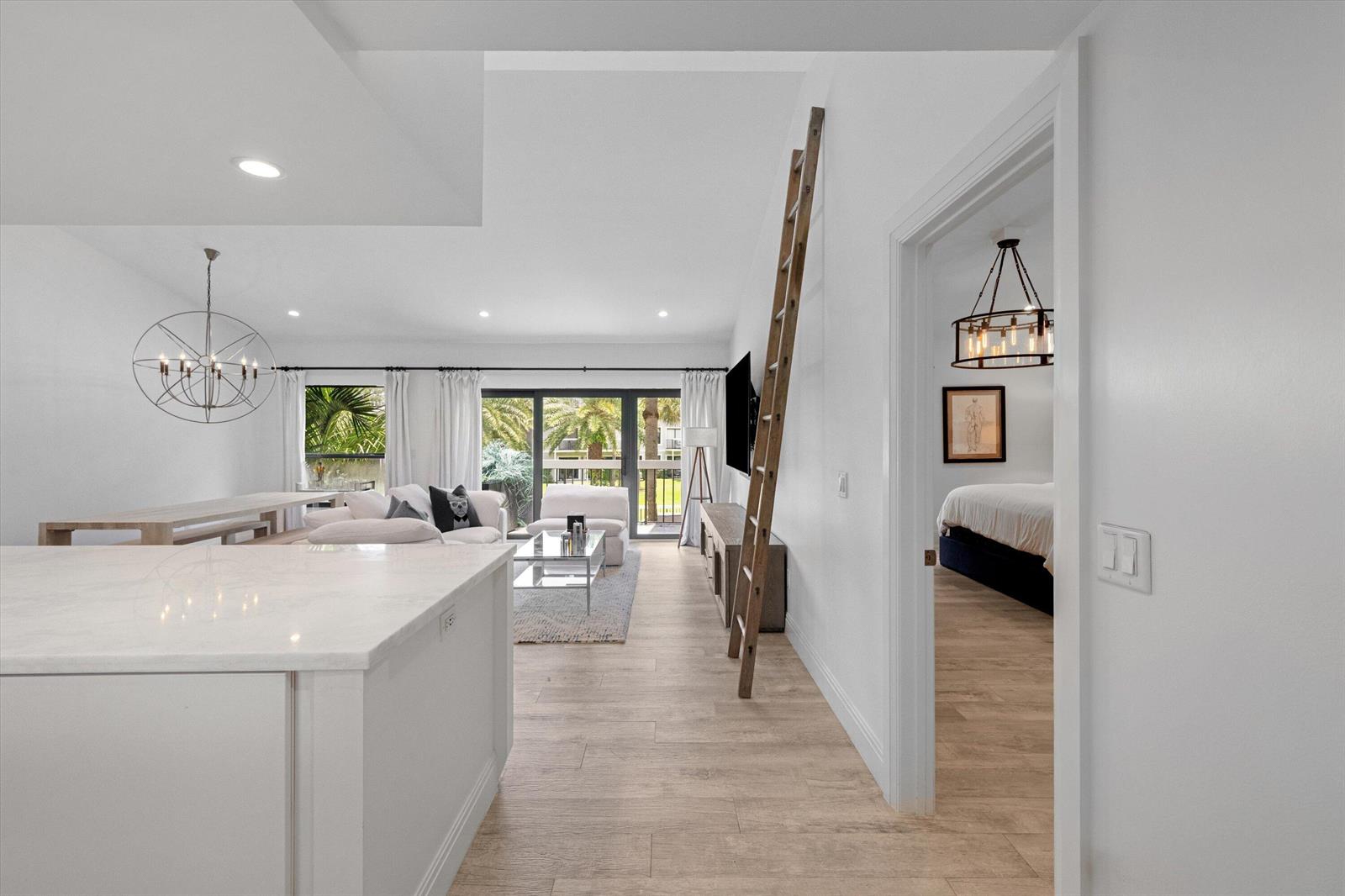 A bright living area with a wooden ladder, white walls, and a view of palm trees — 11863 Wimbledon Circle # 532, Wellington FL 33414, WELLINGTON, FL