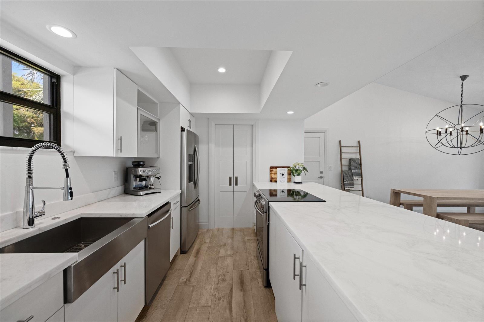 A modern kitchen features white cabinetry, marble countertops, stainless steel appliances, and wood-look flooring — 11863 Wimbledon Circle # 532, Wellington FL 33414, WELLINGTON, FL