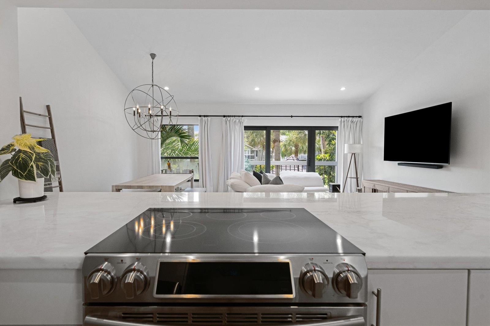 A kitchen island with a glass cooktop overlooks a living and dining area with balcony views — 11863 Wimbledon Circle # 532, Wellington FL 33414, WELLINGTON, FL