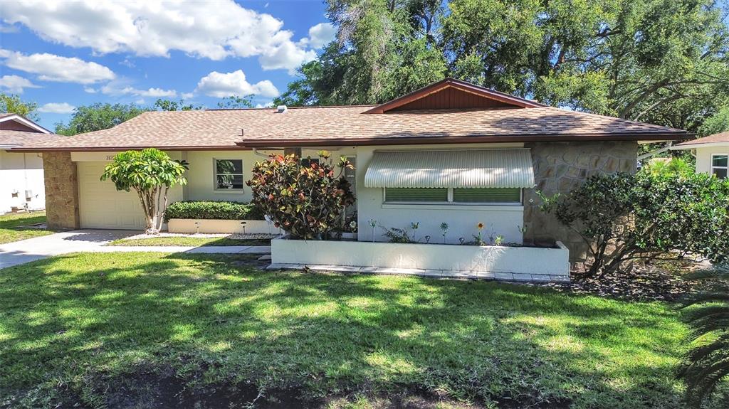 A single-story house with a stone facade, a shingled roof, and a front garden bed — 2819 THISTLE COURT S, PALM HARBOR, FL