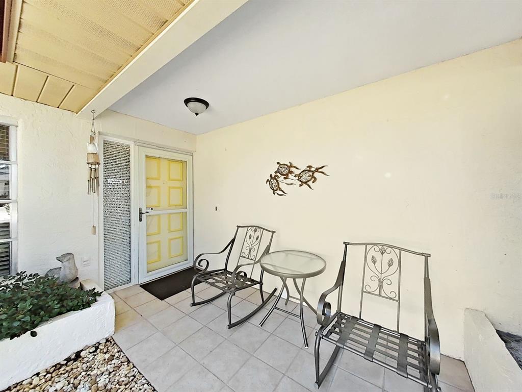 A covered porch features a yellow front door, two metal rocking chairs, and a small table — 2819 THISTLE COURT S, PALM HARBOR, FL