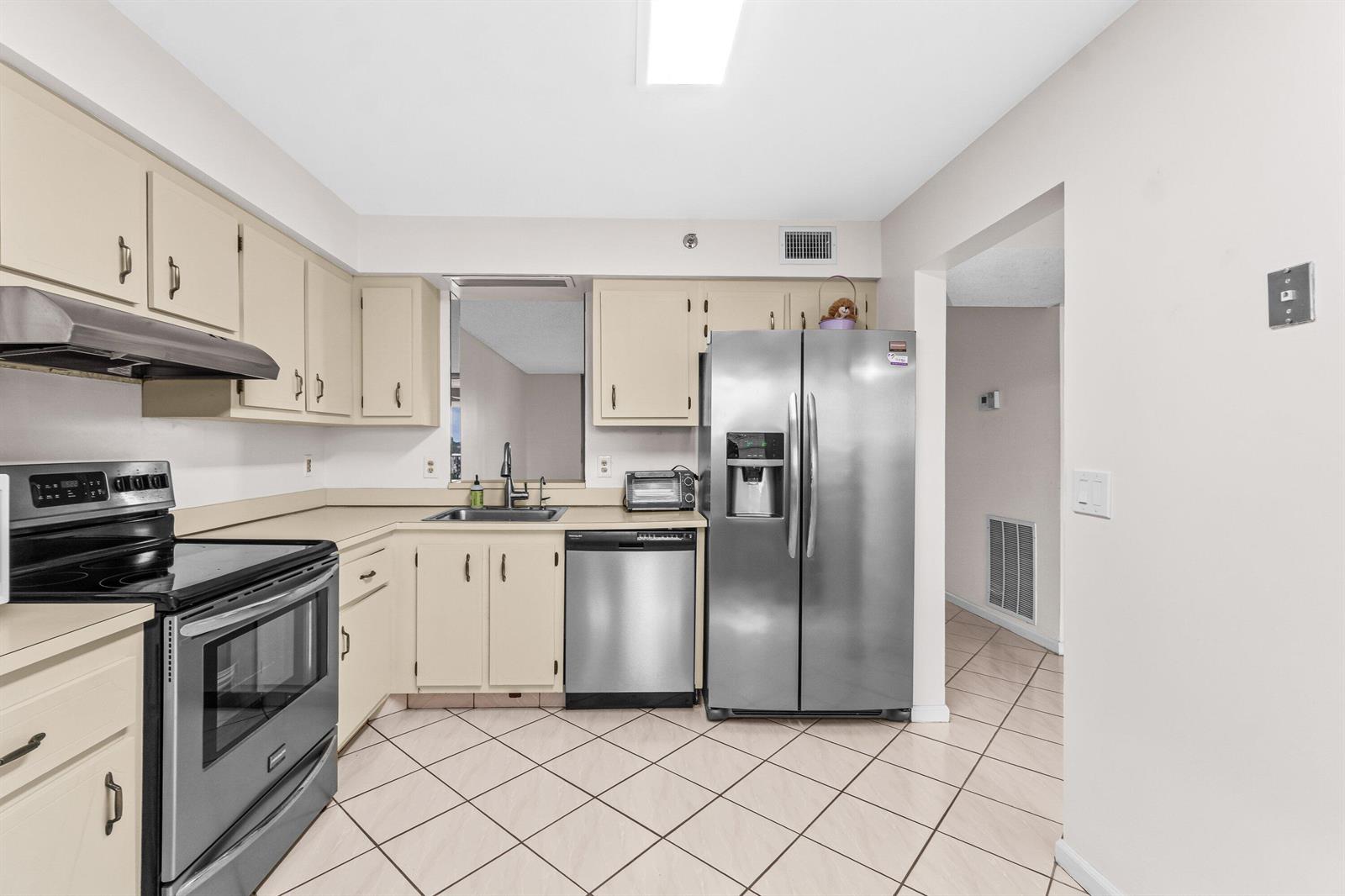 A kitchen features beige cabinets, stainless steel appliances, and light-colored tile flooring — 14623 Bonaire Boulevard # 608, Delray Beach FL 33446, DELRAY BEACH, FL