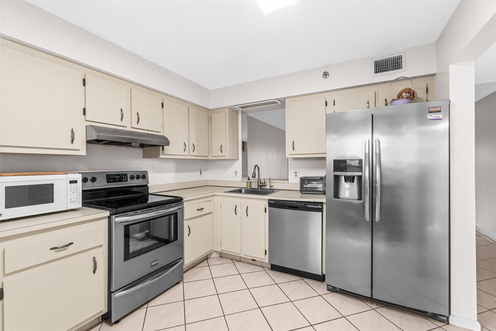 A kitchen features off-white cabinets, stainless steel appliances, and light-colored tile flooring — 14623 Bonaire Boulevard # 608, Delray Beach FL 33446, DELRAY BEACH, FL