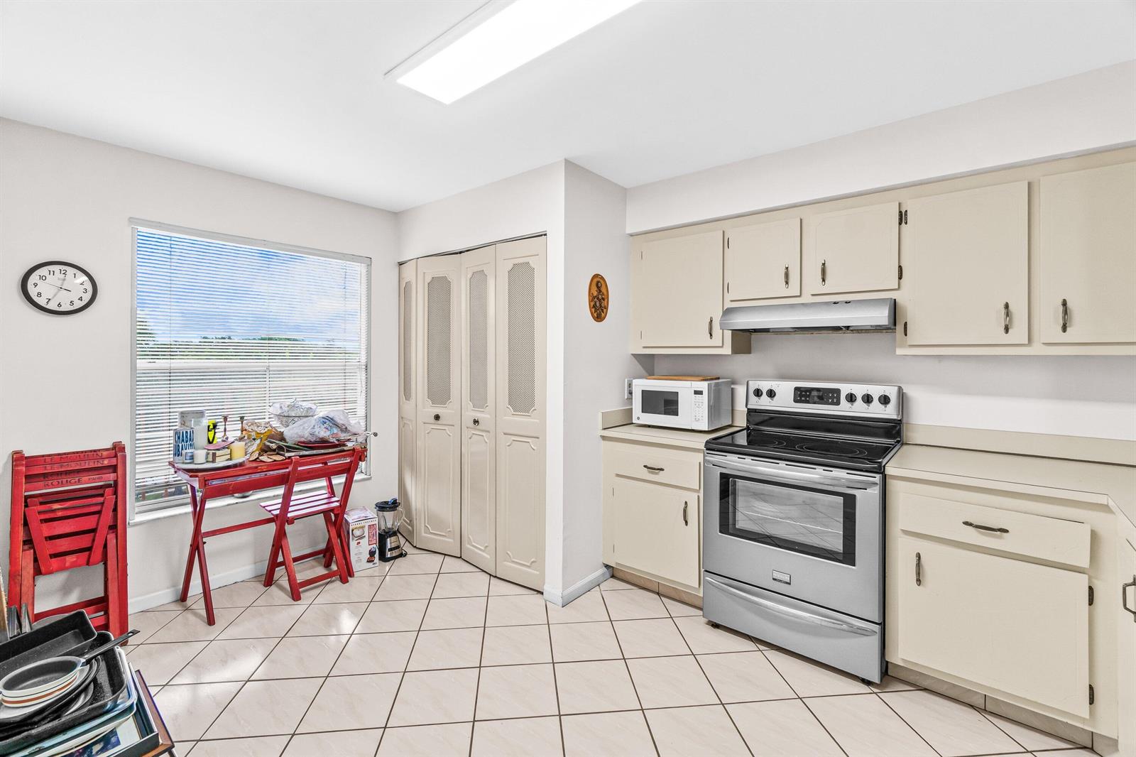 A kitchen features beige cabinets, stainless steel appliances, tile flooring, and a small dining area — 14623 Bonaire Boulevard # 608, Delray Beach FL 33446, DELRAY BEACH, FL