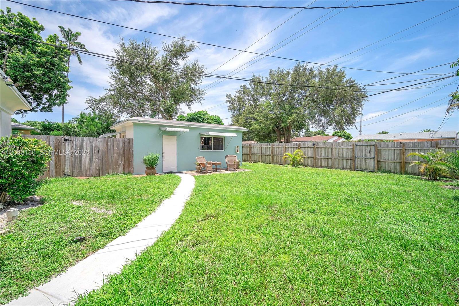 A small, light-green detached building sits in a grassy backyard enclosed by a wooden fence — 261 SW 15th St # 1, Dania Beach FL 33004, DANIA BEACH, FL
